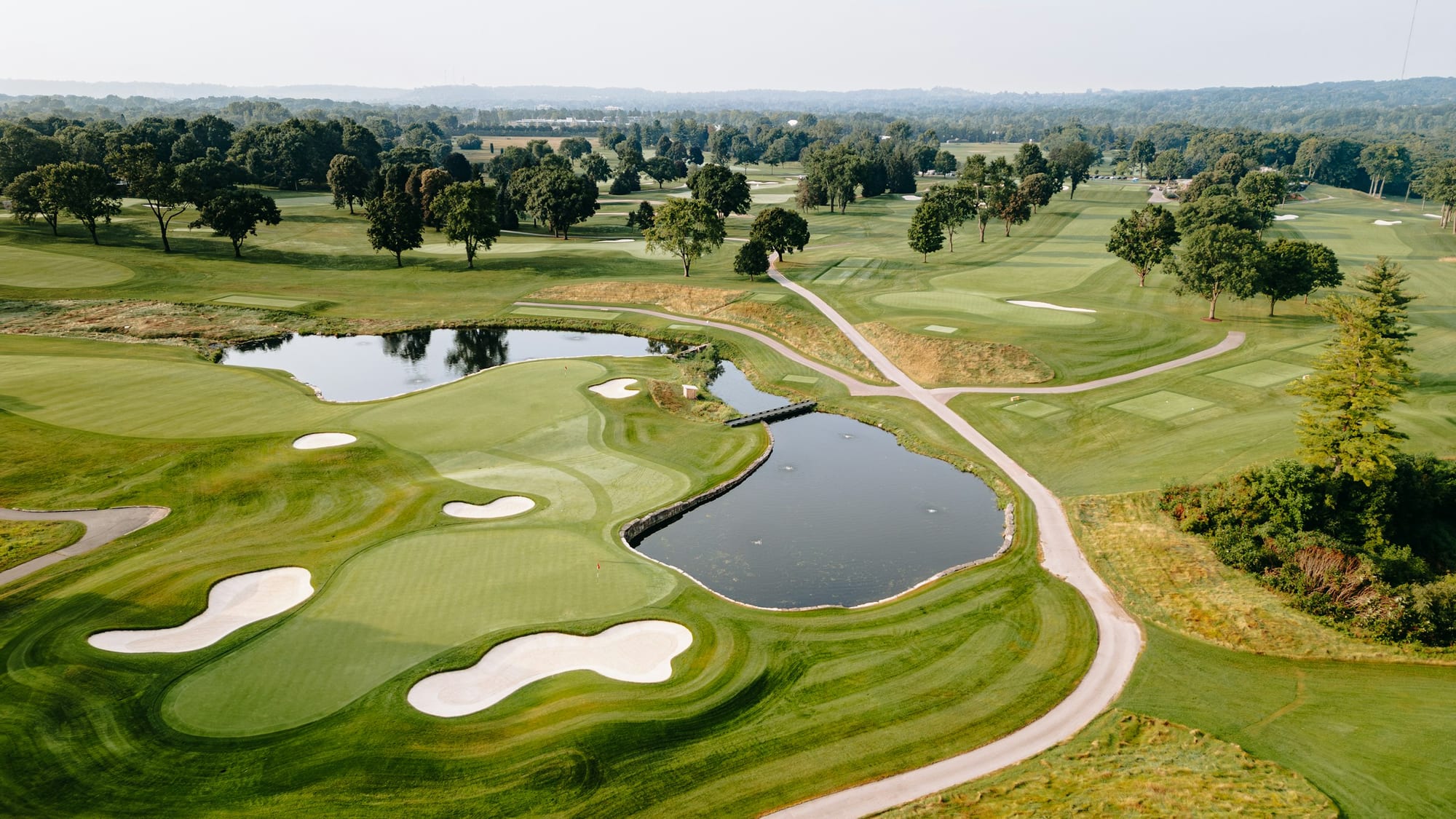 Aerial view of a manicured golf course with fairways, bunkers, and a water hazard