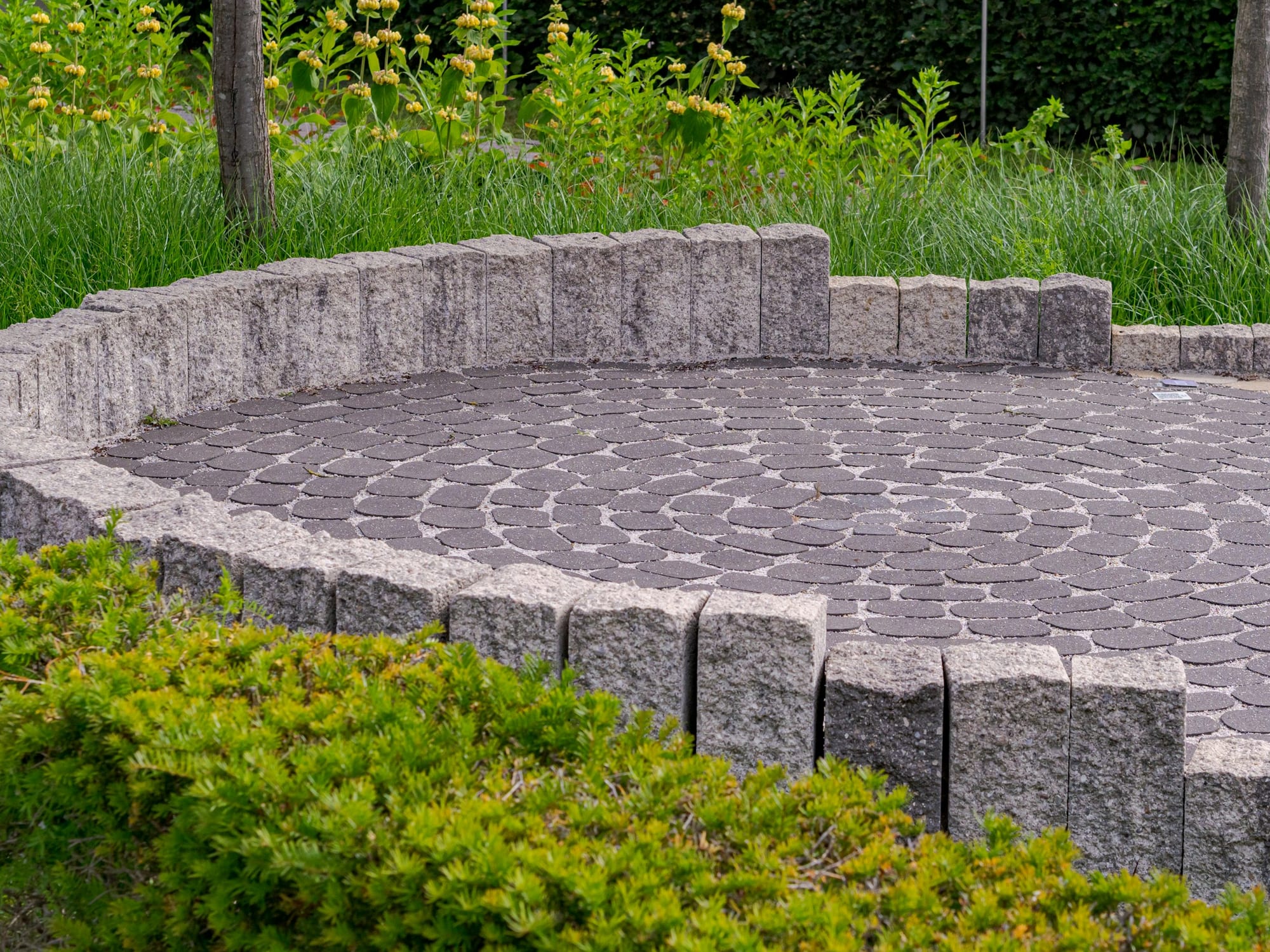 Circular stone paver patio bordered by granite edging and garden beds