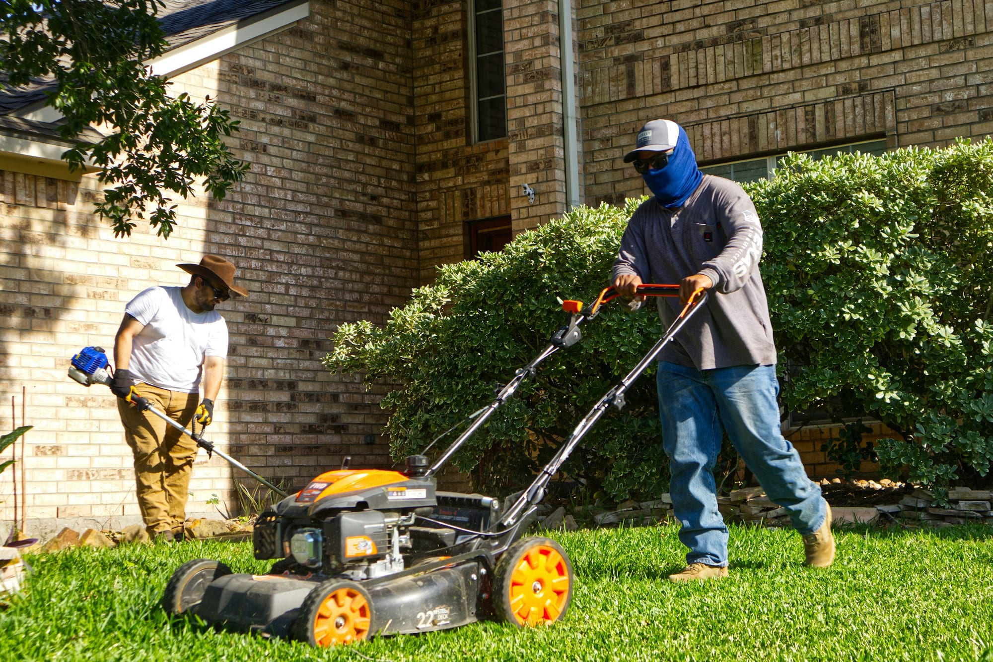 Two-person landscaping crew mowing and trimming a residential lawn
